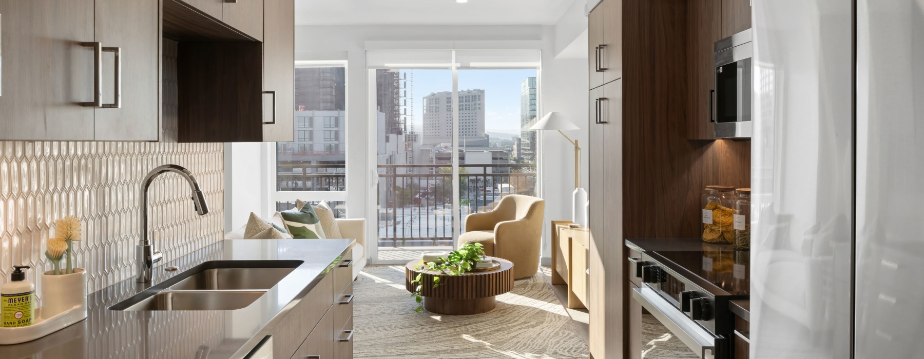 Sleek apartment kitchen at Broadstone Saratoga featuring wood cabinetry, tile backsplash, stainless steel appliances, and open living space with city views.